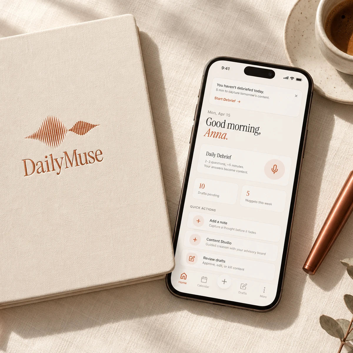 Ein cremefarbenes DailyMuse-Notizbuch, ein Handy mit der App, ein Kupferfüller und Kaffee auf Leinen