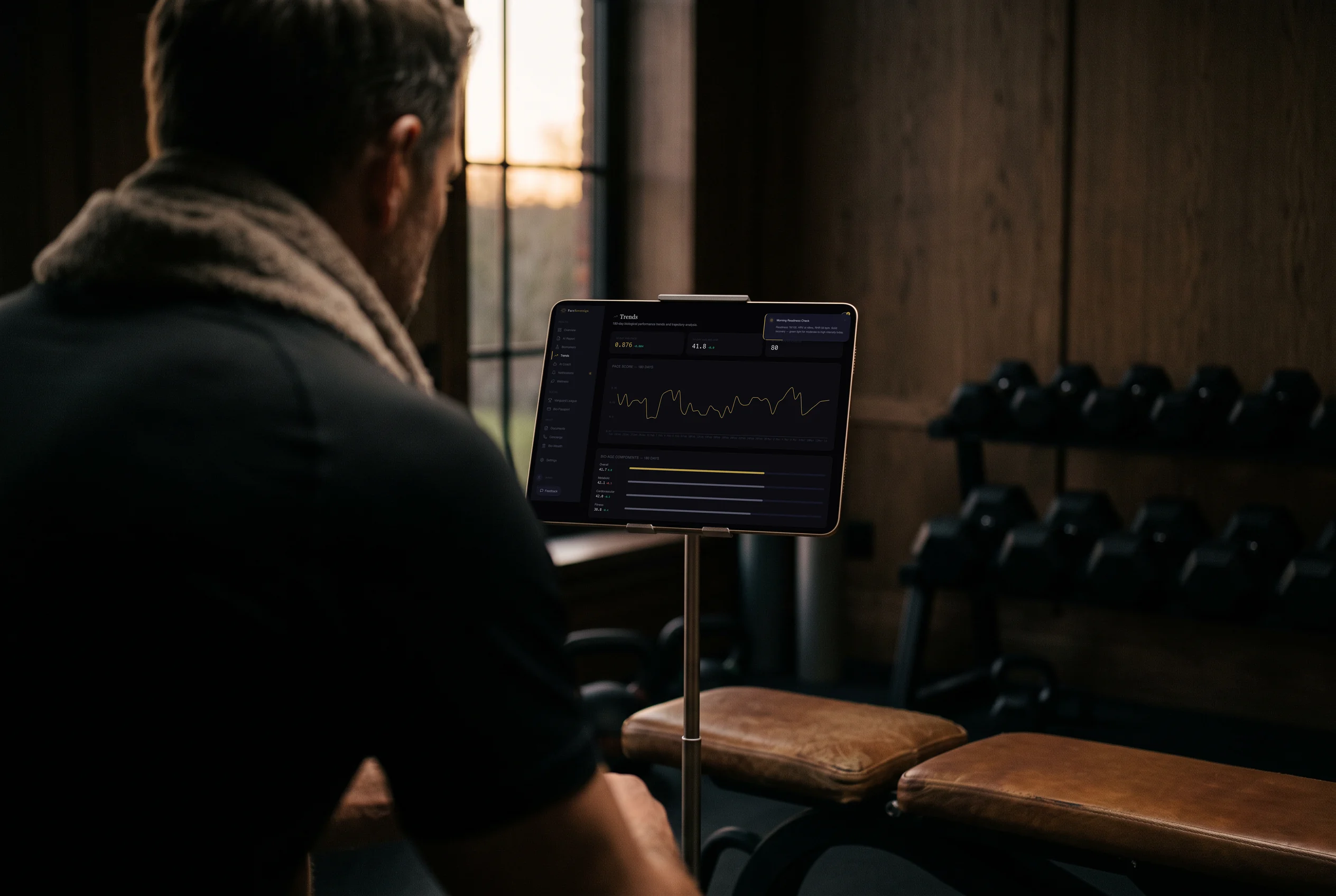 Ein Mann ruht im Morgengrauen auf einer Lederbank in seinem privaten Fitnessraum und prüft auf einem Tablet seine PaceSovereign-Trends